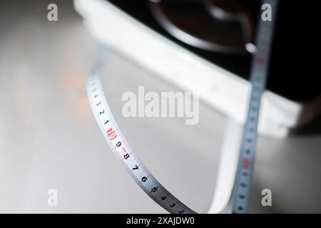 Gros plan d'un ruban à mesurer blanc avec des marques noires et rouges, partiellement enroulé sur une surface blanche. L'arrière-plan est flou, se concentrant sur la bande Banque D'Images