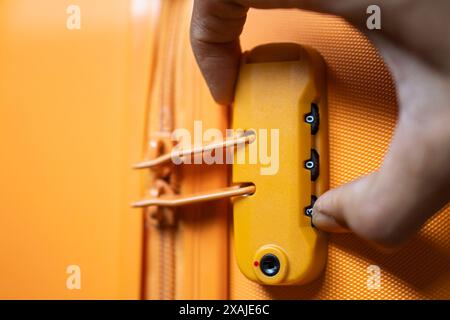 Gros plan d'une personne posant une serrure à combinaison sur une valise jaune. Banque D'Images