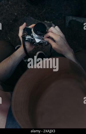 Jeune homme avec chapeau brun ajustant un appareil photo vintage film à l'extérieur Banque D'Images