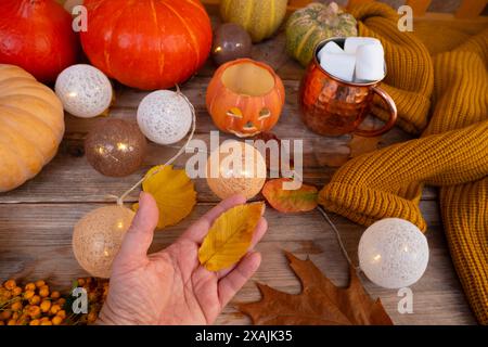 Décor de citrouilles, feuille jaune dans la main féminine, décor d'automne et créativité, chandelier de citrouille Jack avec bougie, décorations d'automne pour Halloween Banque D'Images