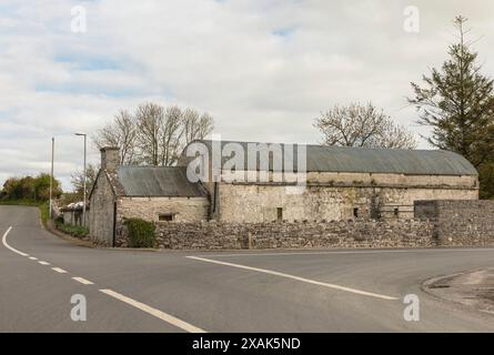 Ancien toit ondulé courbé en fer sur une grange en pierre au coin d'une jonction de route Banque D'Images