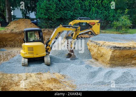 Lors de l'excavation d'irrégularités sur un chantier de construction, une excavatrice remplit les irrégularités avec une base de gravats de granit pour laquelle des fondations en béton sont posées. Banque D'Images