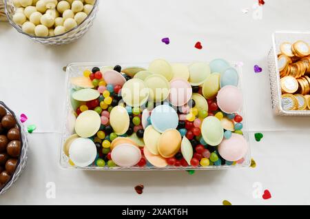 Délicieuses gaufrettes texturées colorées à côté d'autres bonbons dans un récipient en plastique sur une table. Banque D'Images