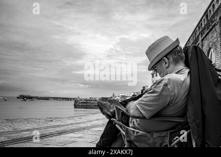 Homme assis et dormant dans une chaise face au port de Swanage. Vacances traditionnelles en bord de mer. Image en noir et blanc. Évocateur. Paisible. Banque D'Images