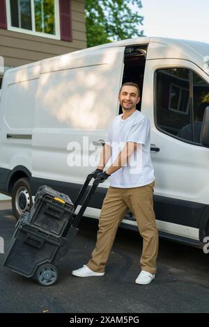 Souriant travailleur d'entrepreneur caucasien dans ses années 40 chargement de ses boîtes à outils dans sa camionnette commerciale. Thème véhicules commerciaux. Banque D'Images
