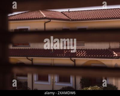 Vue sur les stores de fenêtre : une photo horizontale d'une maison italienne de deux étages en Sardaigne, encadrée à travers les stores de fenêtre d'une fenêtre de l'autre côté de la rue. Banque D'Images