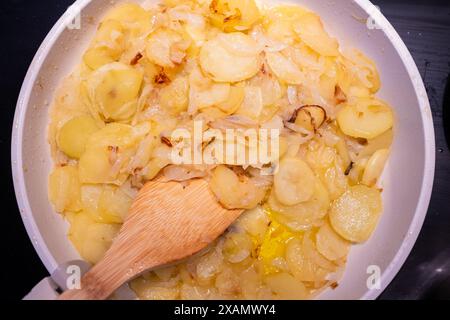 Une assiette de pommes de terre fraîches et d'oignon est frite dans une poêle en granit blanc. cuillère en bois pour un plat bio, écologique, naturel, sain et délicieux. I Banque D'Images