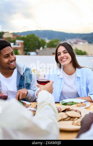 Jeune multiracial beau couple souriant assis à table à un repas d'été amical à l'extérieur. Banque D'Images