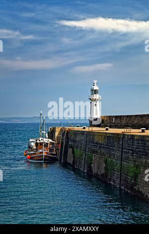 Royaume-Uni, Cornouailles, mur du port extérieur de Mevagissey et phare. Banque D'Images