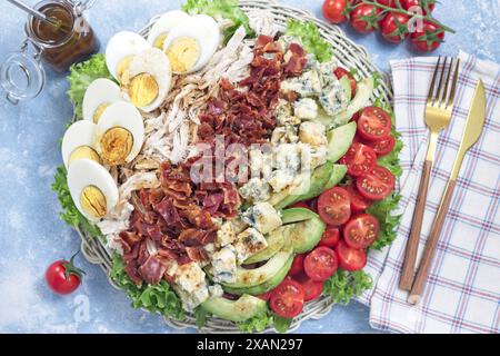 Salade Cobb avec légumes verts, tomate, avocat, fromage bleu, bacon, poulet rôti et œufs durs, sauce vinaigrette, sur une assiette blanche, vue de dessus horizontale Banque D'Images