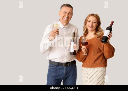 Couple mature avec des bouteilles et des verres de vin sur fond blanc Banque D'Images