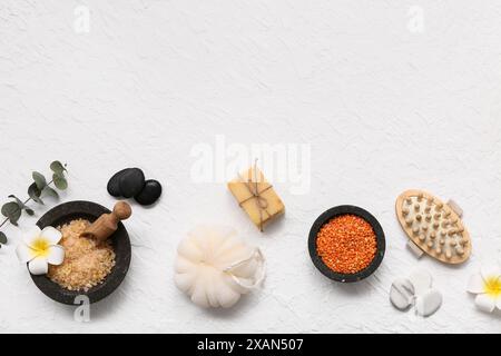 Composition avec des bols de sel de mer, éponge de bain, pierres de spa, barres de savon et fleurs sur fond blanc Banque D'Images