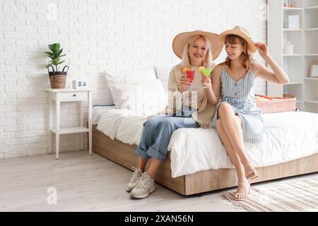 Mère et fille assis sur le lit avec des cocktails dans la chambre. Concept de voyage Banque D'Images