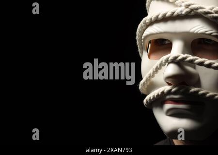 Représentation théâtrale. Homme avec masque en plastique et corde de chanvre sur fond noir, espace pour le texte Banque D'Images