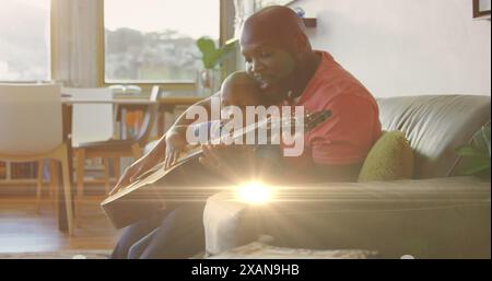 Image de taches lumineuses sur heureux père afro-américain jouant de la guitare avec son fils Banque D'Images