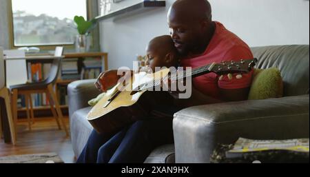 Image de taches lumineuses sur heureux père afro-américain jouant de la guitare avec son fils Banque D'Images