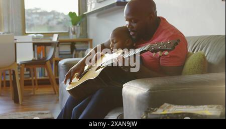 Image de taches lumineuses sur heureux père afro-américain jouant de la guitare avec son fils Banque D'Images