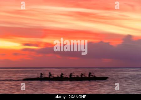 Une image floue de mouvement de pagayeurs en canoë-balancier au coucher du soleil sur la baie de Tumon, Guam, Micronésie., îles Mariannes, mer des Philippines. Banque D'Images