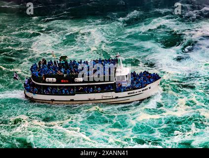 Bateau touristique Maid of the Mist luttant à travers l'eau lourde au pied des chutes du Niagara avec des passagers couverts d'imperméables en plastique bleu Banque D'Images