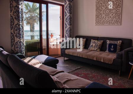 Chambre confortable avec canapé et balcon avec vue sur la mer. Intérieur confortable dans un style marin. Salle de séjour avec décor et mobilier élégants. Canapé avec oreillers. Banque D'Images