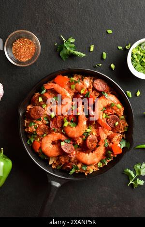 Jambalaya de style créole avec des crevettes, des saucisses fumées et des légumes dans une poêle en fonte sur fond sombre. Vue de dessus, pose à plat, gros plan Banque D'Images