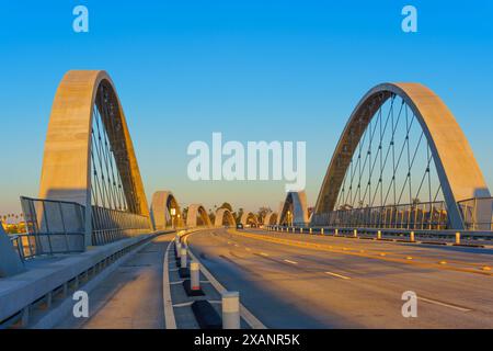 Le pont moderne arbore des arcs distinctifs et se dresse contre un ciel bleu clair, capturé lors d'un moment de coucher de soleil serein sans certains véhicules présents Banque D'Images