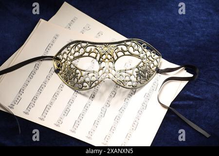 Masque facial élégant et feuilles de musique sur tissu bleu. Représentation théâtrale Banque D'Images