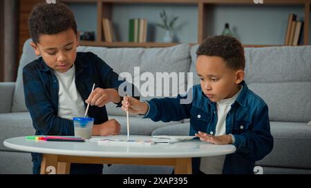 Deux enfants afro-américains enfants écoliers garçons ethniques petits amis frères frères peignant ensemble à la maison avec des peintures aquarelles colorées Banque D'Images