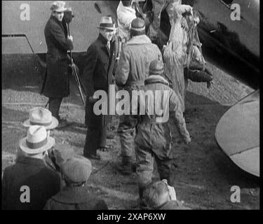 L'aviateur américain Charles Augustus Lindbergh et sa femme Anne Morrow Lindbergh portant des tenues de pilotes marchant vers leur avion surveillé par une petite foule et des membres de la presse, dans les années 1930 L'affaire d'enlèvement de bébé Lindbergh de 1932 - "le crime du siècle". « Le premier voyageur solo de l'Atlantique est à l'apogée de sa renommée. Ensemble, lui et sa femme Anne Morrow Lindbergh continuent de tracer la piste de leur aviation bien-aimée. De "Time to Remember - The Tough Guys", années 1930 (Reel 2) ; film ddocumentaire, principalement sur la vie dans la dépression et les gangsters américains. Banque D'Images