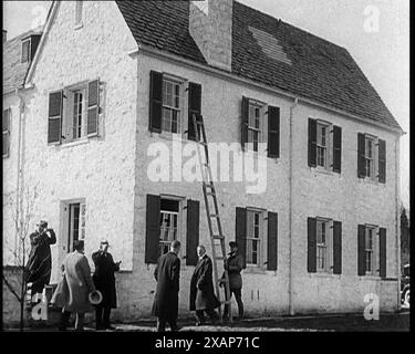 Civils américains masculins devant la maison de l'aviateur américain Charles Augustus Lindbergh enquêtant sur un enlèvement, une échelle est vue contre une fenêtre, années 1930 L'affaire d'enlèvement de bébé Lindbergh de 1932 - "le crime du siècle". "Une fenêtre ouverte, une échelle, et le garçon Lindbergh est parti... une des recherches les plus grandes et les plus approfondies de l'histoire peigne la zone autour de la maison Lindbergh [dans le New Jersey]... Une simple maison en bois devient le centre du monde...". De "Time to Remember - The Tough Guys", années 1930 (Reel 2) ; film documentaire, principalement sur la vie en dépression Banque D'Images