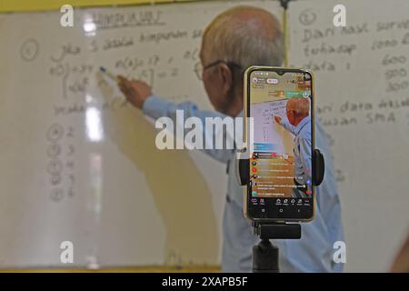 7 juin 2024, Purworejo, Java central, Purworejo : MELAN Achmad (78) un professeur de mathématiques à la retraite enseigne et apprend toujours en utilisant les médias sociaux avec l'aide de son fils comme vidéaste via téléphone portable à son domicile de Purworejo, Java central. MELAN Achmad, communément appelé Mbah Matematika, est à la retraite depuis 2003, mais son enthousiasme pour le partage des connaissances n'a jamais été éteint en utilisant les médias sociaux TikTok appelés ''˜@binaprestasiwa' pour atteindre les étudiants en partageant des matériaux mathématiques pour le primaire, le collège et le lycée, et en discutant des questions de test d'entrée à l'université. MBA Banque D'Images