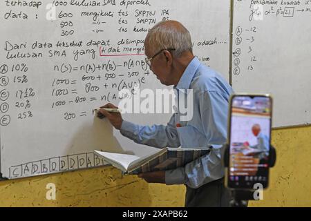 7 juin 2024, Purworejo, Java central, Purworejo : MELAN Achmad (78) un professeur de mathématiques à la retraite enseigne et apprend toujours en utilisant les médias sociaux avec l'aide de son fils comme vidéaste via téléphone portable à son domicile de Purworejo, Java central. MELAN Achmad, communément appelé Mbah Matematika, est à la retraite depuis 2003, mais son enthousiasme pour le partage des connaissances n'a jamais été éteint en utilisant les médias sociaux TikTok appelés ''˜@binaprestasiwa' pour atteindre les étudiants en partageant des matériaux mathématiques pour le primaire, le collège et le lycée, et en discutant des questions de test d'entrée à l'université. MBA Banque D'Images