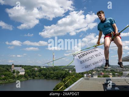 08 juin 2024, Saxe, Chemnitz : Slackliner Ruben Langer a attaché une bannière à un haut-parleur au-dessus de l'étang Schlossteich à Chemnitz avec le slogan "la démocratie a besoin de courage! - Allez voter'. La slackline de 630 mètres de long est tendue entre la tour de l'église du château (à l'arrière) et un immeuble de grande hauteur et est considérée comme la plus longue ligne dans les zones urbaines en Allemagne. Les slackliners veulent utiliser la campagne pour promouvoir les élections européennes et locales de dimanche. La ligne s'étend sur les terrains du festival de la démocratie 'Kosmos'. Selon les organisateurs, un total de plus de 200 articles de programme seront Banque D'Images