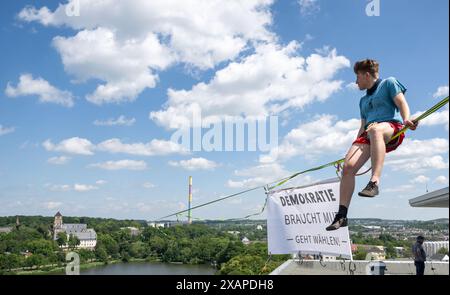 08 juin 2024, Saxe, Chemnitz : Slackliner Ruben Langer a attaché une bannière à un haut-parleur au-dessus de l'étang Schlossteich à Chemnitz avec le slogan "la démocratie a besoin de courage! - Allez voter'. La slackline de 630 mètres de long est tendue entre la tour de l'église du château (à l'arrière) et un immeuble de grande hauteur et est considérée comme la plus longue ligne dans les zones urbaines en Allemagne. Les slackliners veulent utiliser la campagne pour promouvoir les élections européennes et locales de dimanche. La ligne s'étend sur les terrains du festival de la démocratie 'Kosmos'. Selon les organisateurs, un total de plus de 200 articles de programme seront Banque D'Images