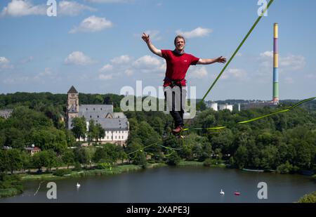 08 juin 2024, Saxe, Chemnitz : Jens Decke se balance à une hauteur de 50 mètres sur une ligne haute au-dessus de l'étang du château à Chemnitz. La slackline de 630 mètres de long est tendue entre la tour de l'église du château (à l'arrière) et un immeuble de grande hauteur et est considérée comme la plus longue ligne dans une zone urbaine en Allemagne. Les slackliners passent un peu moins de 45 minutes sur un tronçon. La ligne s'étend sur les terrains du festival de la démocratie 'Kosmos'. Selon les organisateurs, un total de plus de 200 articles du programme seront offerts en une journée. Environ 50 000 visiteurs sont attendus au festival. Photo Banque D'Images