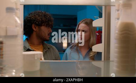 Point de vue POV à l'intérieur du réfrigérateur fille caucasienne femme petite amie femme et homme arabe gars indien petit ami mari multiracial couple la nuit Banque D'Images