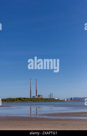 Plage de Sandymount à marée basse avec les cheminées emblématiques de Poolbeg en arrière-plan par une journée ensoleillée. Le ciel est bleu vif contre les cheminées Banque D'Images