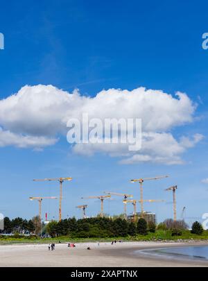 Plage de Sandymount sur une journée lumineuse et ensoleillée avec des grues jaunes en arrière-plan. Il y a quelques nuages dans le ciel bleu vif Banque D'Images