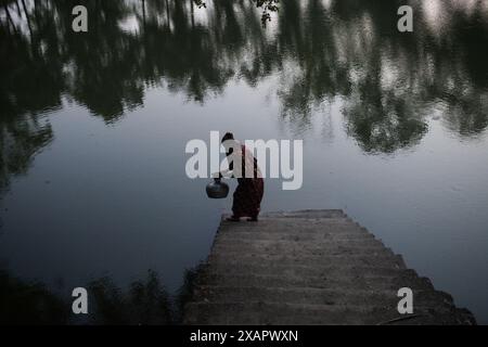 8 juin 2024, Dhaka, Dhaka, BANGLADESH : une femme bangladaise collecte de l'eau potable à partir d'une source d'eau douce, marchant un long chemin pour recueillir de l'eau potable dans la zone côtière de Khulna, au Bangladesh. Selon une étude de l’American Geophysical Union, l’élévation du niveau de la mer, qui affecte la disponibilité de l’eau potable, entraînera la migration d’environ 1,3 millions de personnes à travers le pays d’ici 2050. Une combinaison d'inondations dues aux marées, d'inondations dues aux ondes de tempête et d'intrusion d'eau salée entraîne une augmentation de la salinité dans les eaux souterraines et les étangs d'eau douce, causant une augmentation de la salinité du dr Banque D'Images