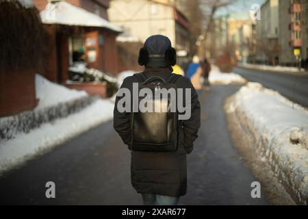 Un homme vêtu de noir dans la rue. Sac à dos et veste noirs. Homme inconnu de derrière. Passer-par en hiver dans la ville. Banque D'Images