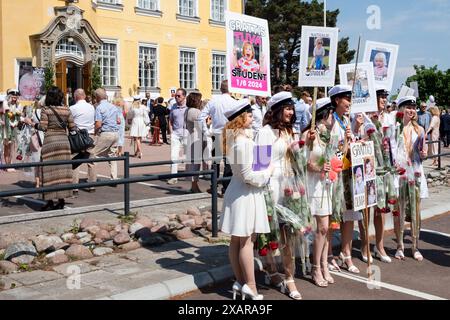 LES FILLES POSENT POUR UNE PHOTO DE GROUPE, REMISE DES DIPLÔMES DE Åland, MARIEHAMN : un grand groupe de jeunes filles diplômées posent pour une photo de célébration avec des fleurs et leurs pancartes de bébé à l'extérieur du bâtiment principal de l'école au jour de la remise des diplômes de Åland 2024 au Lyceum de Åland (gymnase de Ålands) à Mariehamn, archipel de Åland, mer Baltique, Finlande – C’est le jour où les élèves quittent l’école pour la dernière fois. Dans le cadre de cette tradition nordique, des pancartes sont tenues avec des photos de bébé des diplômés et les étudiants eux-mêmes portent leurs chapeaux de graduation de style marin (studentmössa) et s'habillent en costumes et robes blanches. Banque D'Images