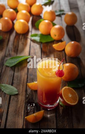 Cocktail classique de tequila au lever du soleil, superposé de tequila aux teintes vibrantes de jus d'orange et de grenadine, garni d'une brochette de cerises maraschino. Banque D'Images