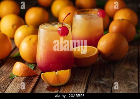 Cocktail classique de tequila au lever du soleil, superposé de tequila aux teintes vibrantes de jus d'orange et de grenadine, garni d'une brochette de cerises maraschino. Banque D'Images