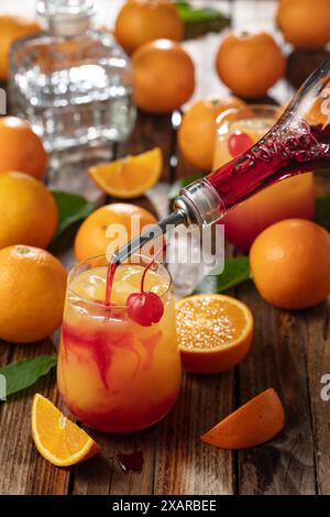 Cocktail classique de tequila au lever du soleil, superposé de tequila aux teintes vibrantes de jus d'orange et de grenadine, garni d'une brochette de cerises maraschino. Banque D'Images