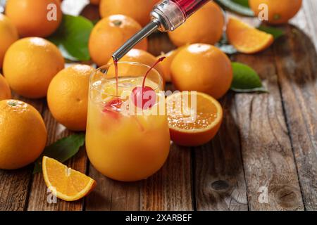 Cocktail classique de tequila au lever du soleil, superposé de tequila aux teintes vibrantes de jus d'orange et de grenadine, garni d'une brochette de cerises maraschino. La grenadine est po Banque D'Images