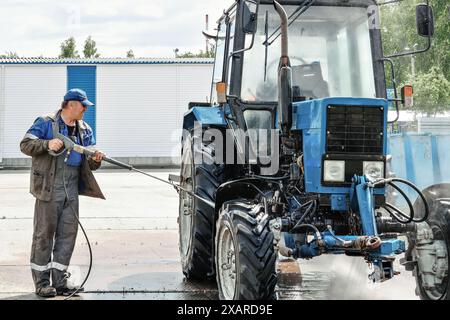 Un homme lave un tracteur avec un nettoyeur haute pression. Le tracteur est bleu et a un gros pneu Banque D'Images