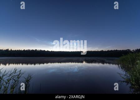 Nuages noctilucents au-dessus du lac forestier en Lettonie dans la nuit de juin Banque D'Images
