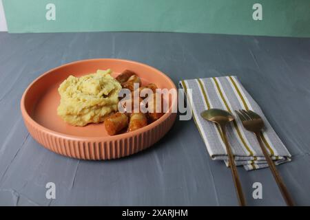 Déjeuner servi : purée de pommes de terre, saucisses avec sauce tomate, fourchette, cuillère sur serviette sur fond gris. Vue latérale. Banque D'Images