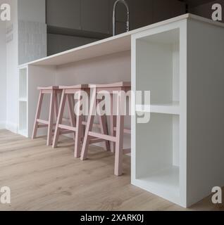 Trois tabourets de bar en bois rose au bar du petit déjeuner de la cuisine dans la salle à manger spacieuse ouverte de la cuisine avec des murs peints en blanc, des armoires de couleur cachemire gris Banque D'Images