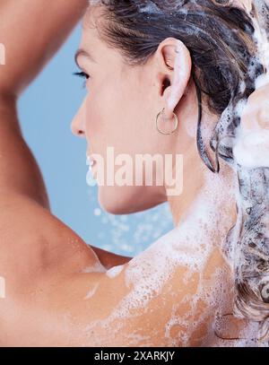 Femme, lavage des cheveux et mousse de shampooing dans le studio, nettoyage et soins capillaires dans la douche sur fond bleu. Femme personne, profil et savon à bulles pour Banque D'Images